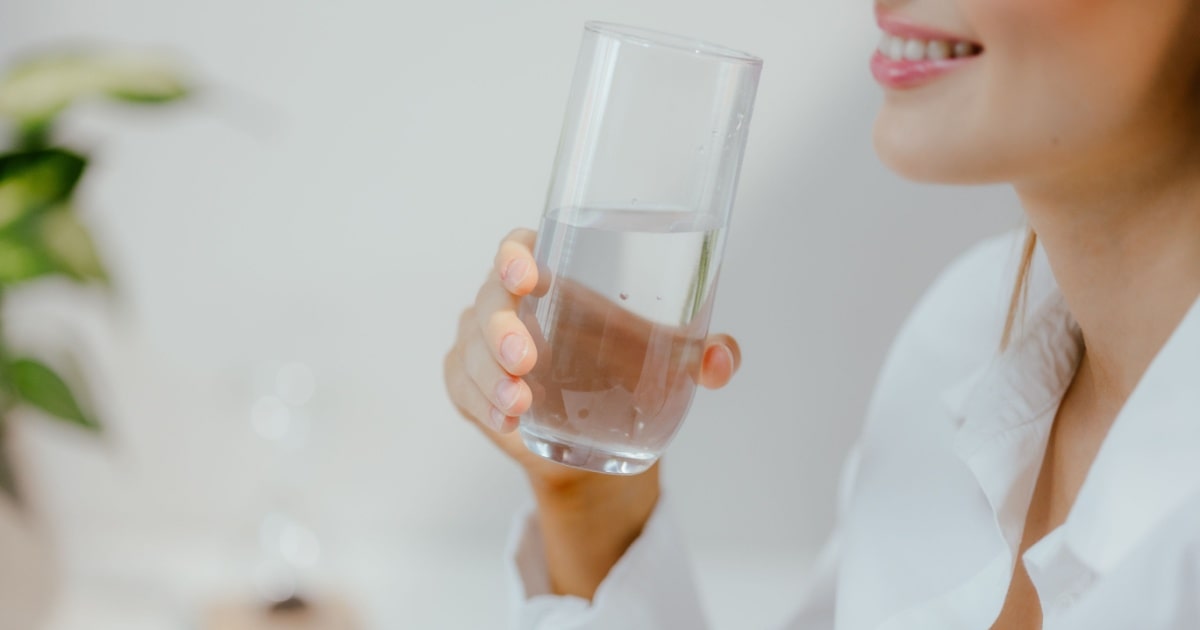 Une femme souriante tient un verre d'eau dans sa main