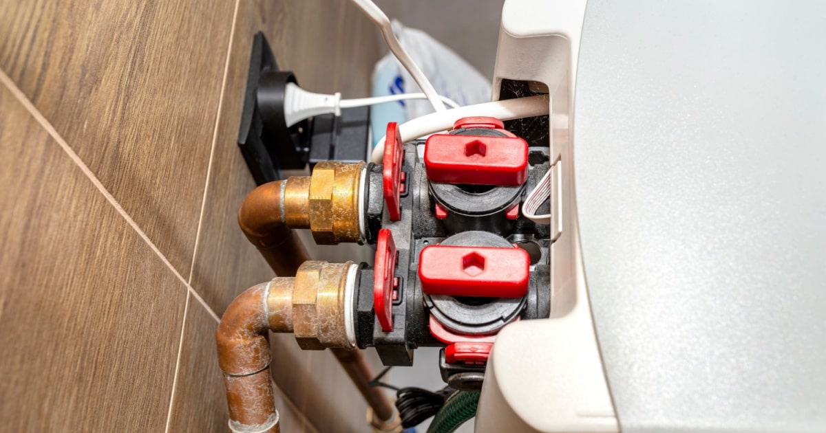Arrière d'un adoucisseur d'eau au sel avec canalisation et branchement électrique fixé au mur.