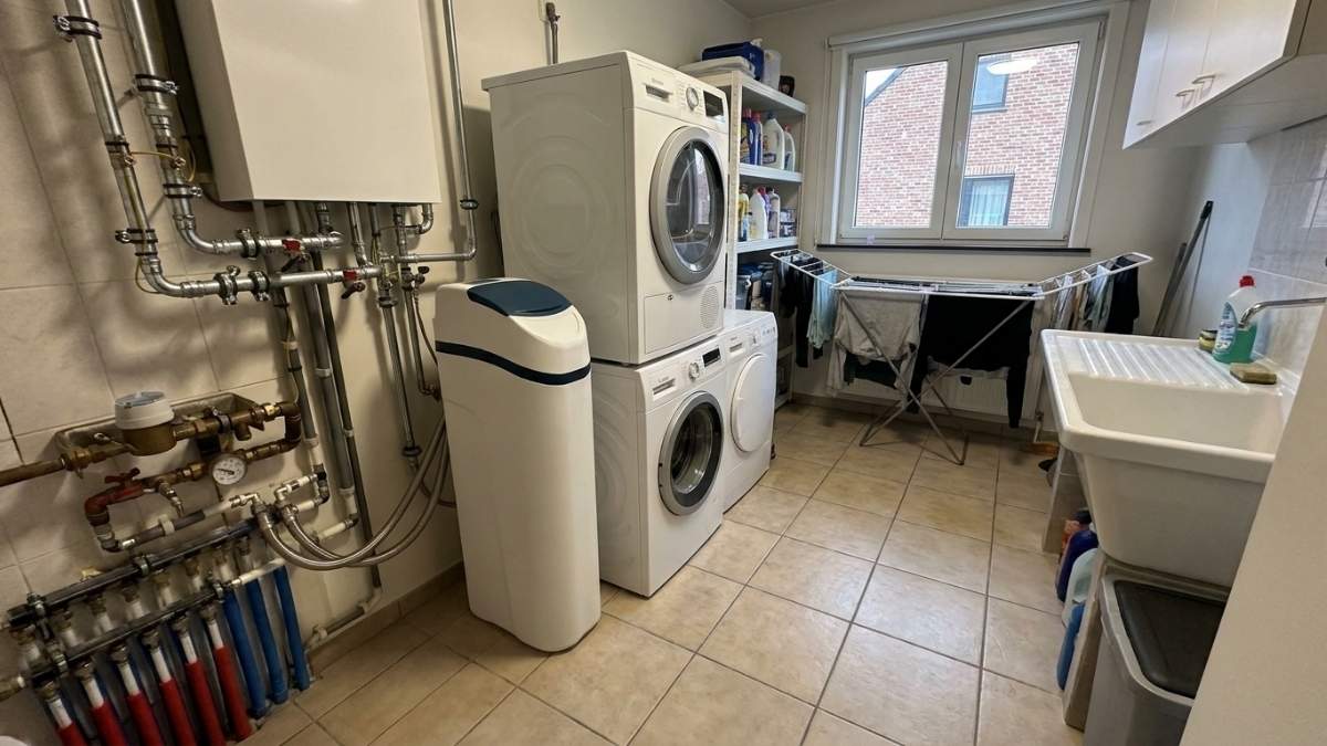 Adoucisseur d'eau blanc type Kalkéo Blue fonctionnant au sel installé sur le sol d'une buanderie avec branchement aux canalisations.