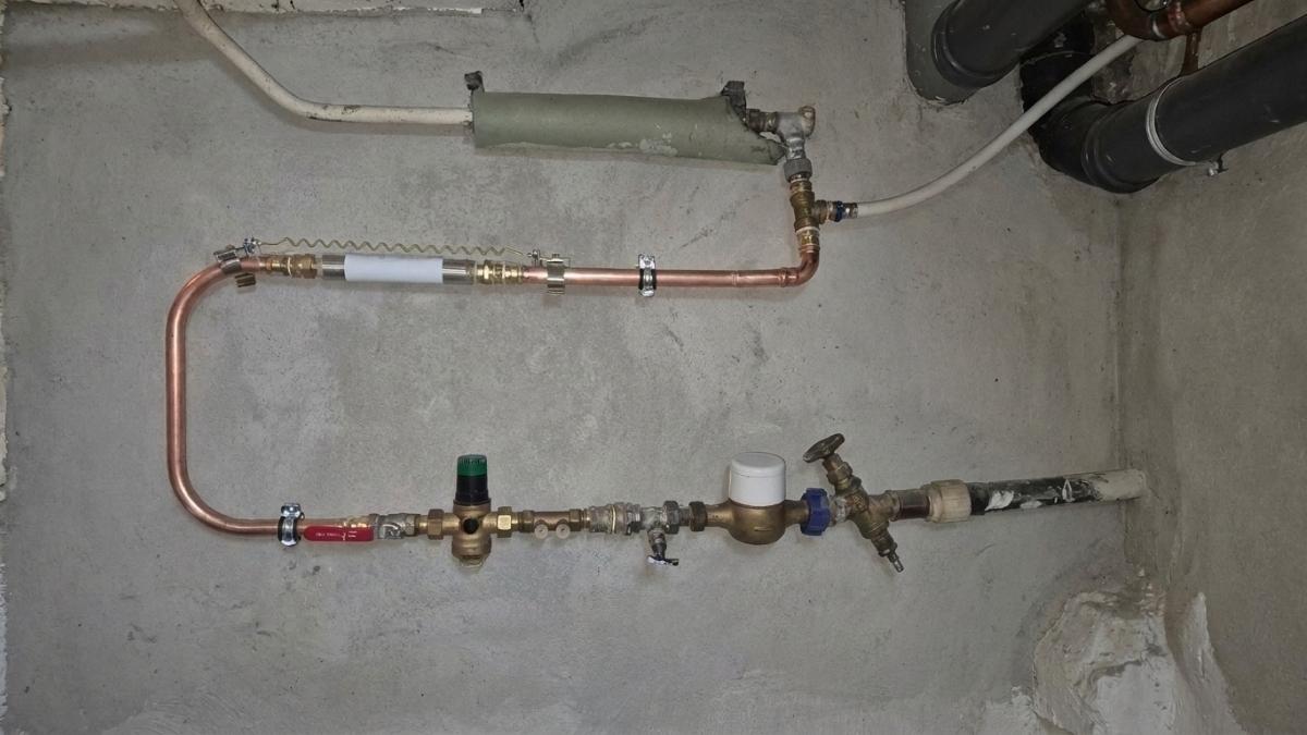 Canalisations dans une cave avec système anti-calcaire type Calcéo et compteur d'eau.